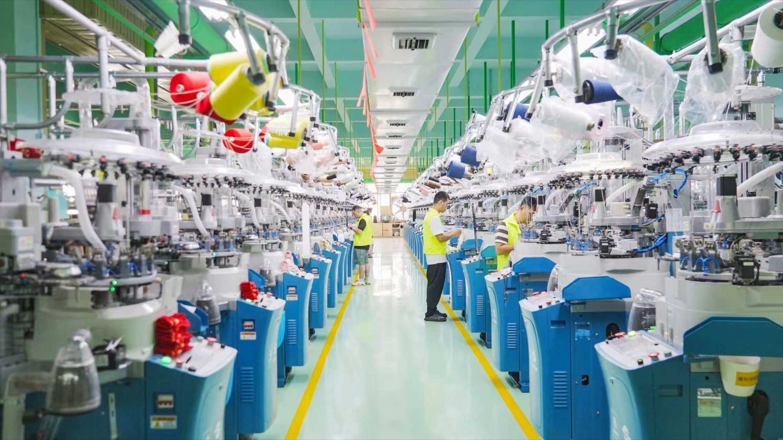 Workers monitor rows of circular knitting machines during sock production.